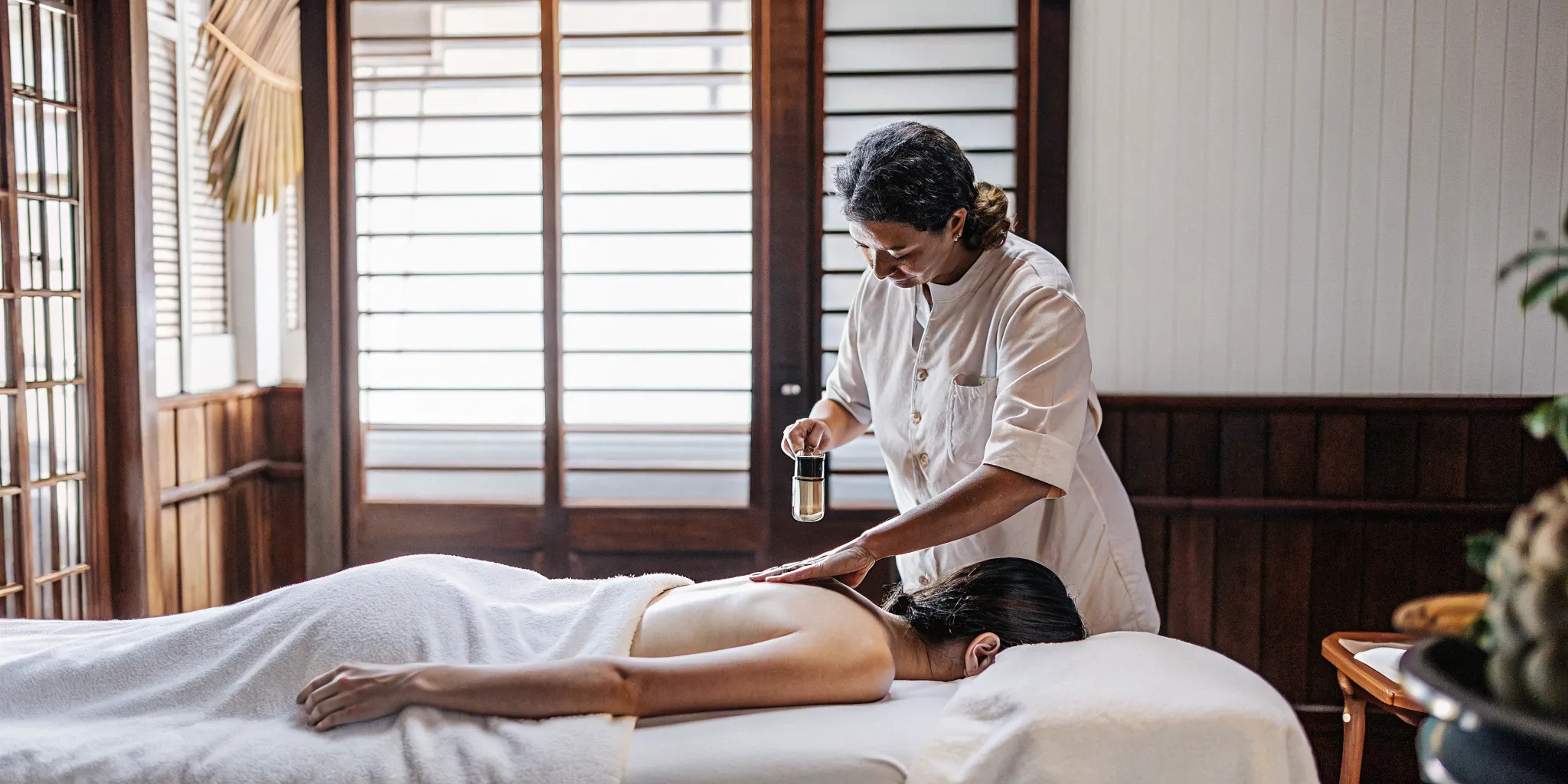Massage therapist applying CBD oil to a guest's shoulders in a warm therapeutic massage studio in New Orleans