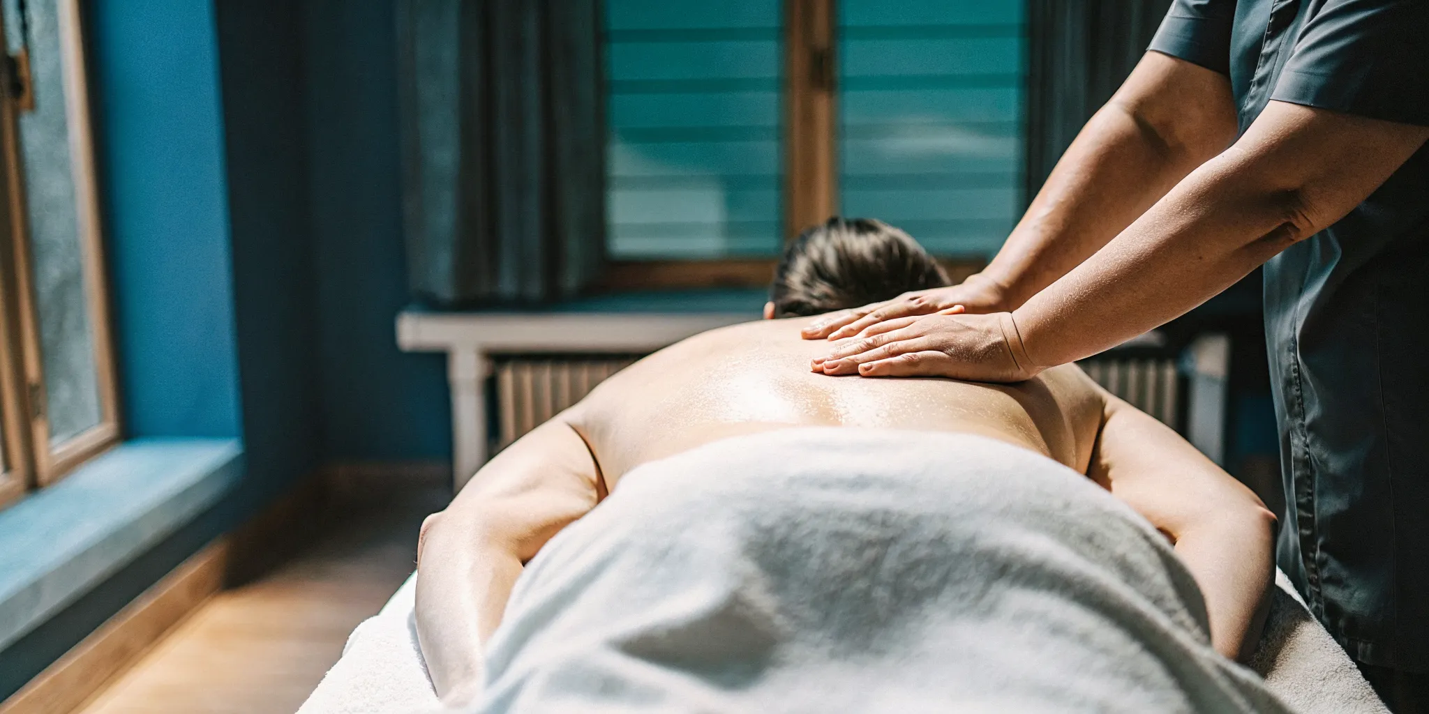 Massage therapist applying therapeutic deep tissue pressure to a guest's upper back in a warm, professional treatment room
