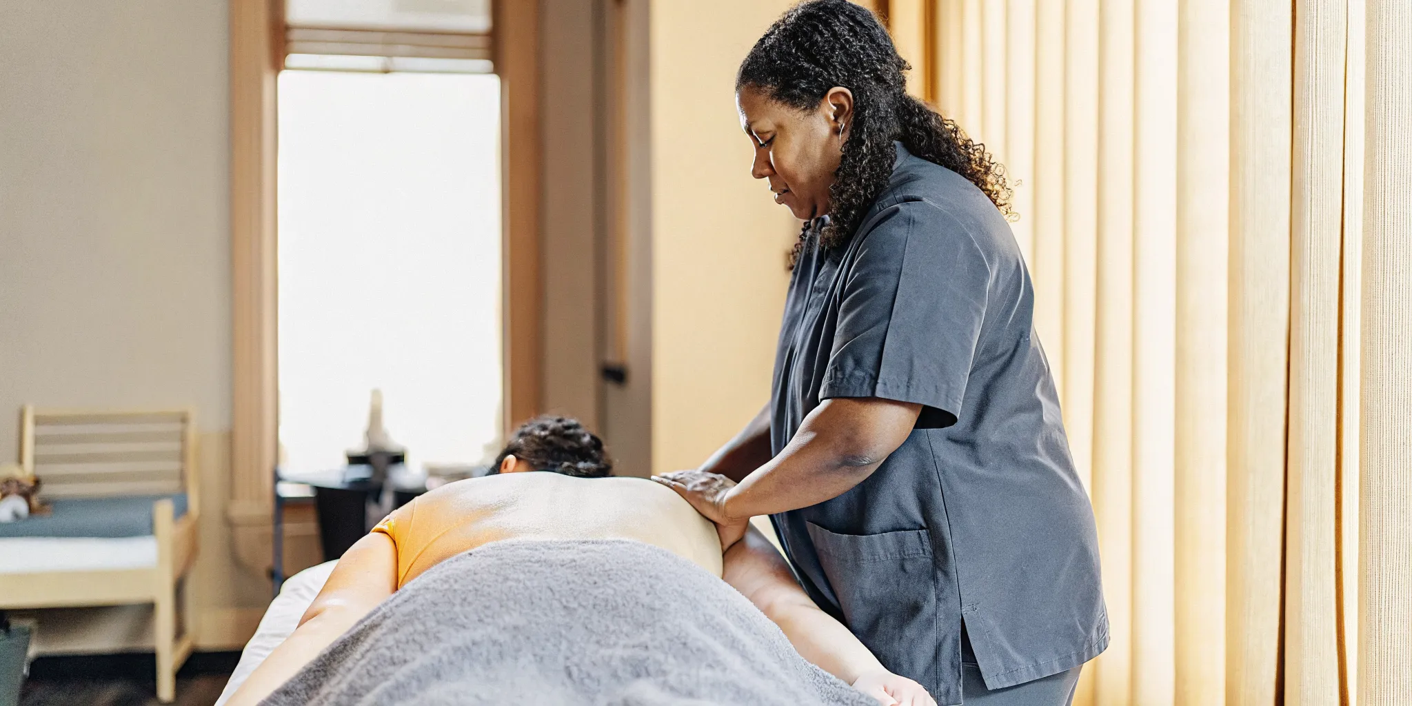 Massage therapist performing Swedish massage with gliding strokes on a guest's back in a warm, professional treatment room
