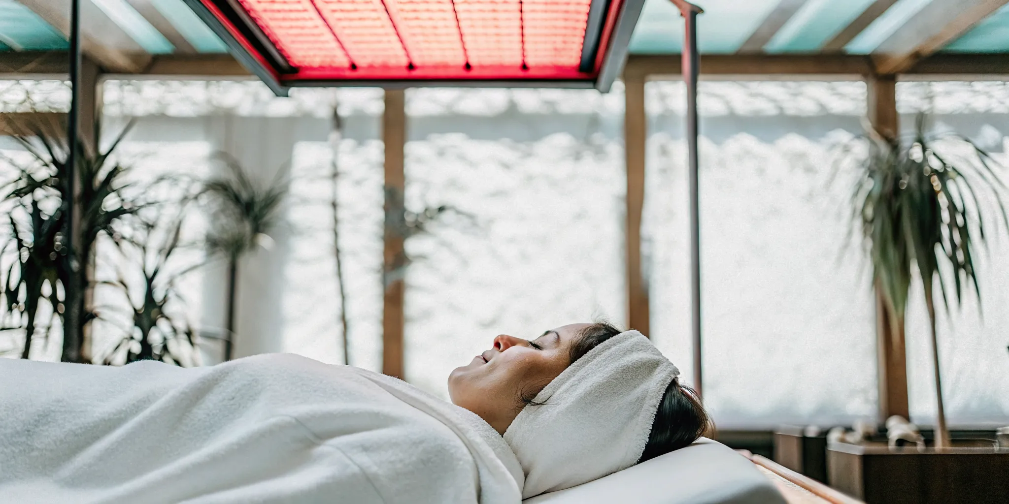 Person lying on a massage table under a red light therapy panel in a warm, calming wellness studio